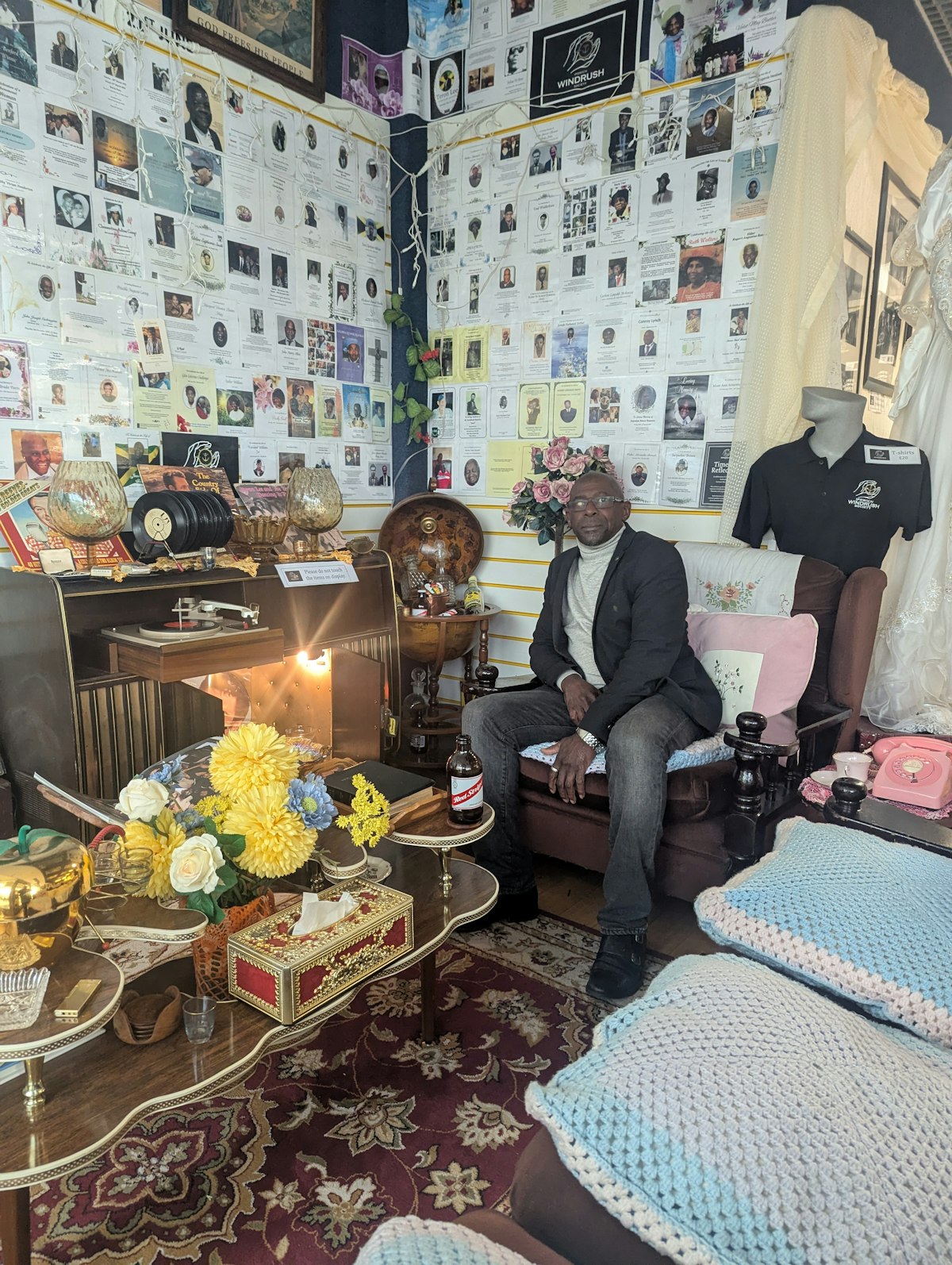 Founder of Ipswich Windrush Society, Max Thomas, seated in the Reflection Room on a sofa, surrounded by cultural artefacts